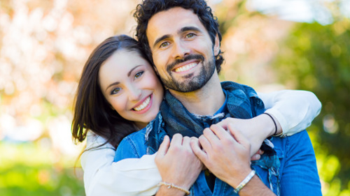 Smiling couple outdoors showing bright, white teeth related to tooth whitening